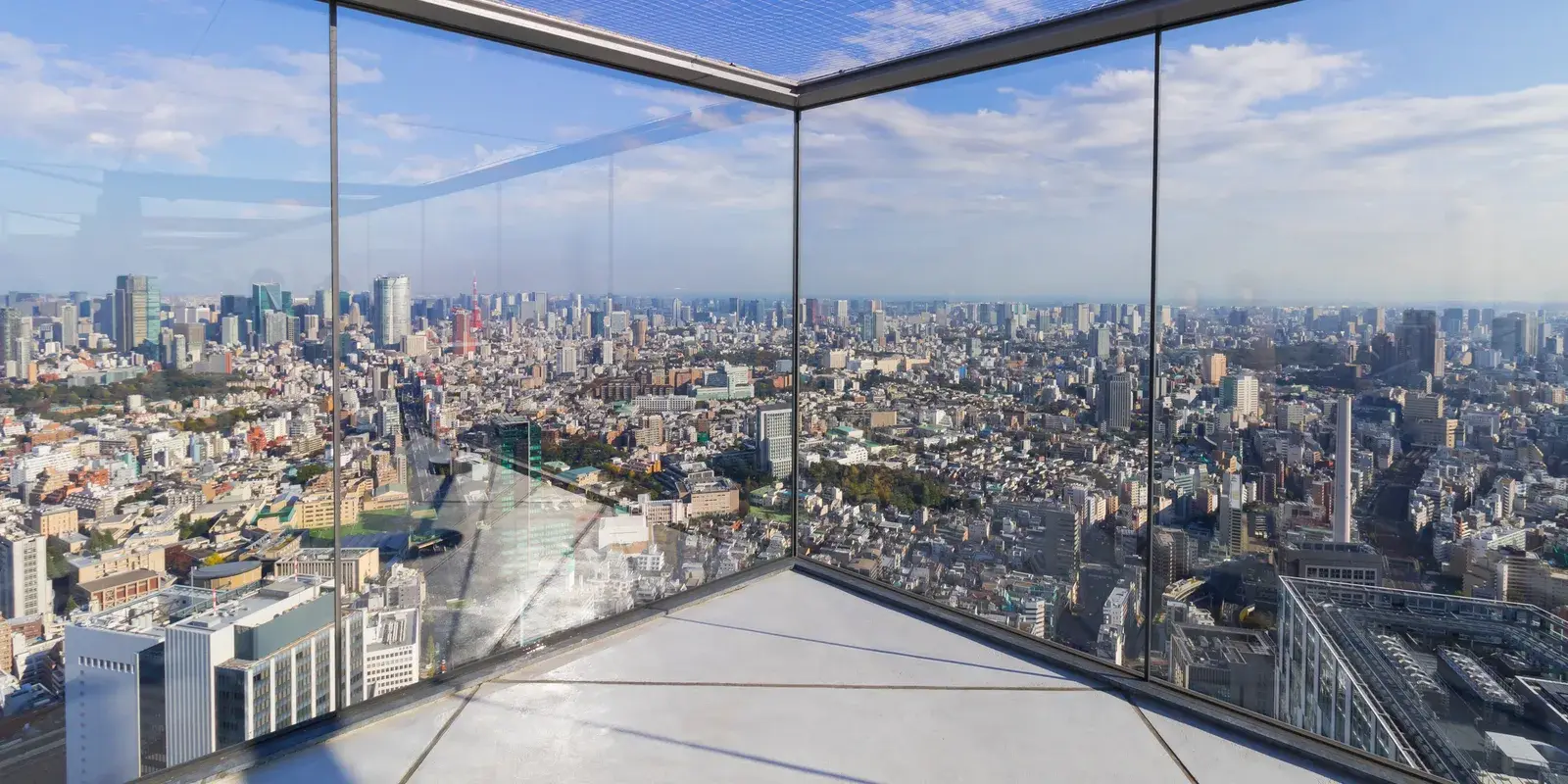 A glass-walled corner of the Shibuya Sky rooftop deck looking out over the Tokyo skyline under a partly cloudy sky