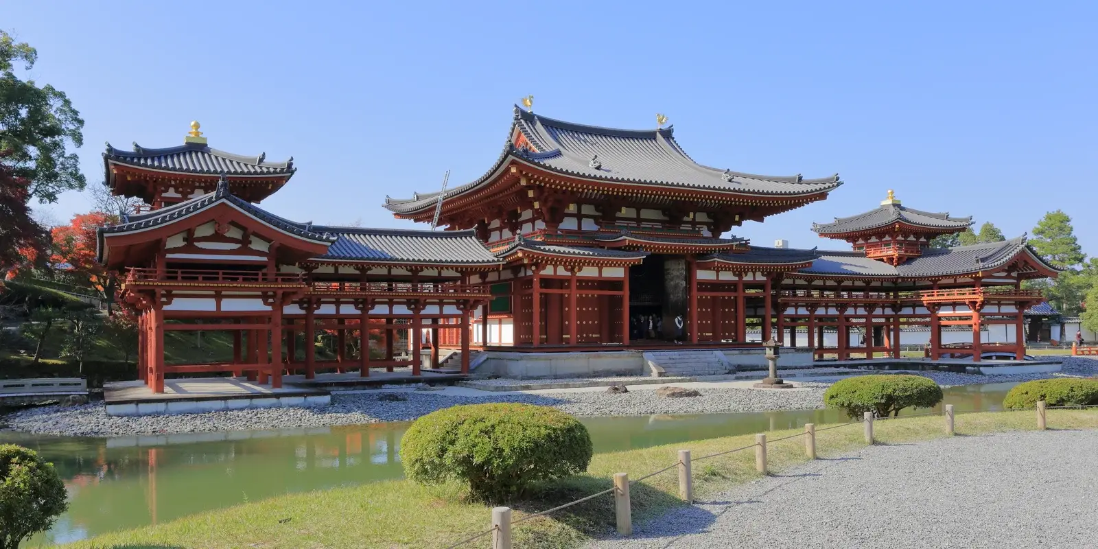 Byodo-in's Phoenix Hall and its wings reflected in the still green water of Aji Pond, seen across the garden on a clear day
