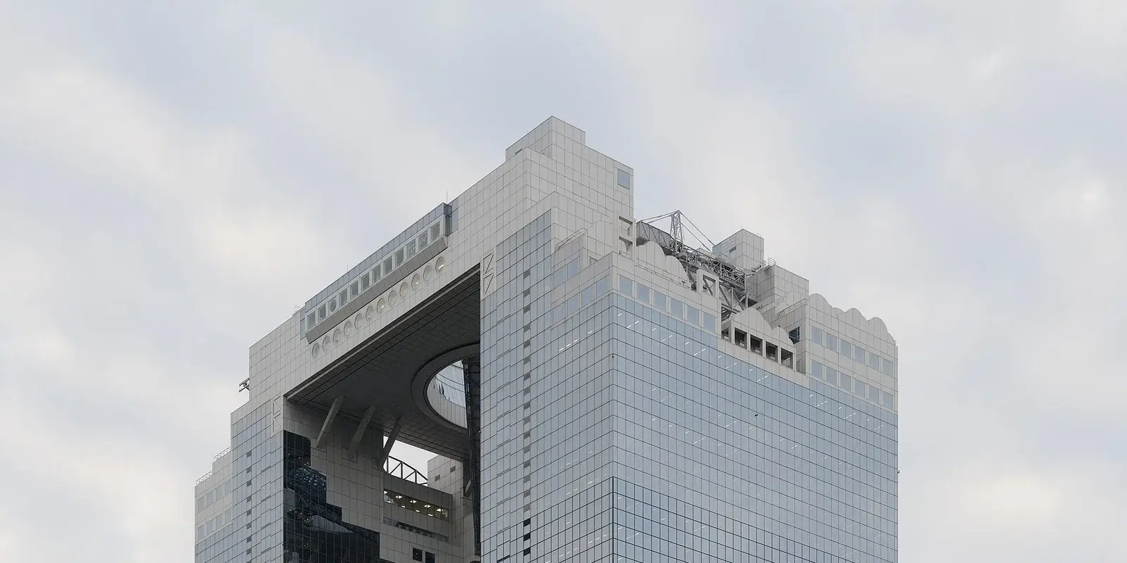 Looking up at the top of Umeda Sky Building, where a ring-shaped glass structure with a circular opening connects the two towers