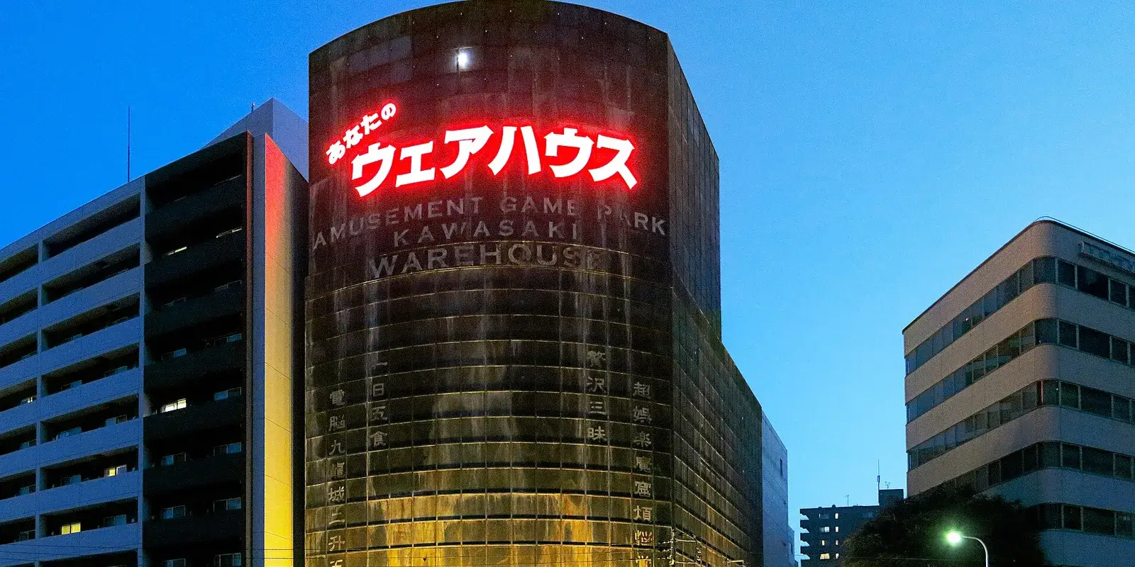 A large illuminated Japanese game center building glowing red at dusk, with no people in view