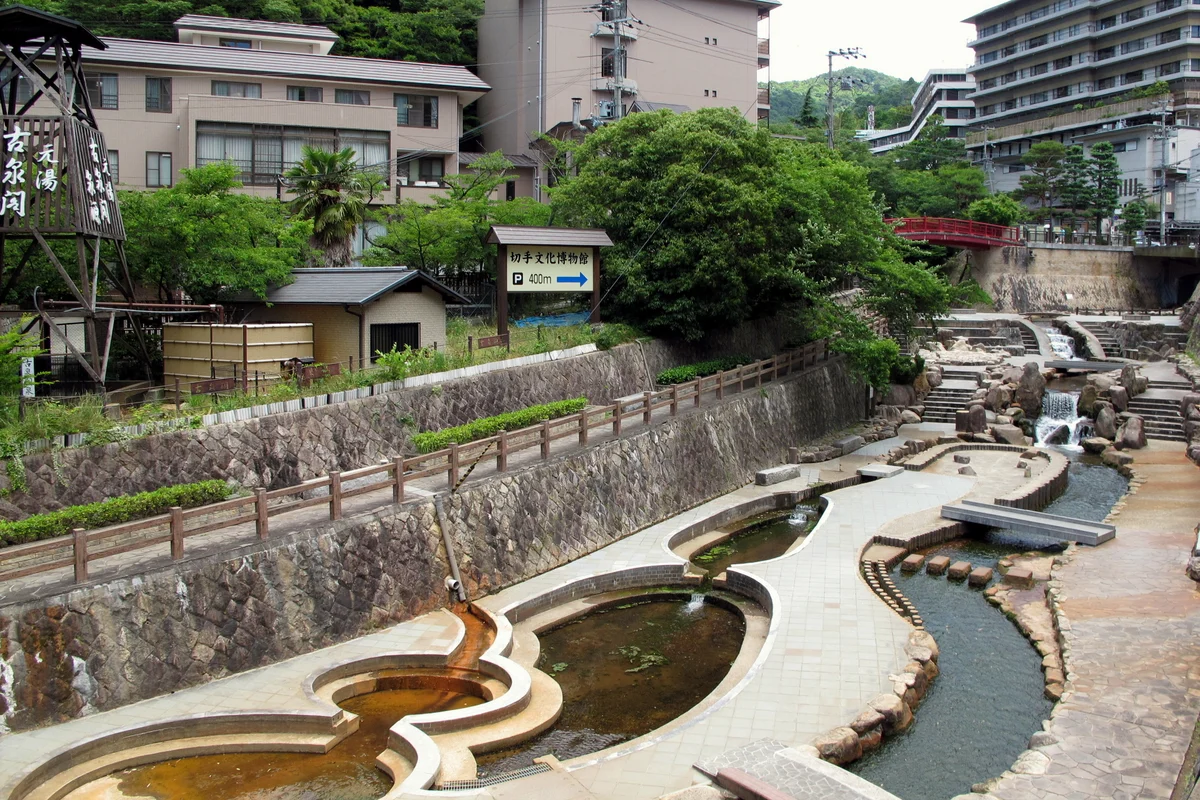 Stone-edged pools and steps along the Arima River in the middle of the onsen town, with hotels on the hillside and a red footbridge upstream