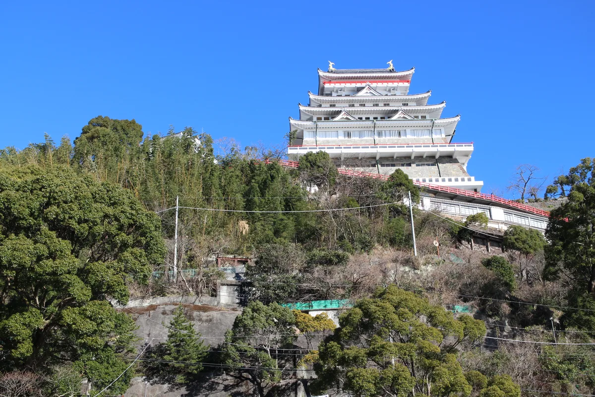 Atami Castle's tiered keep seen from below the hillside, against a clear blue sky
