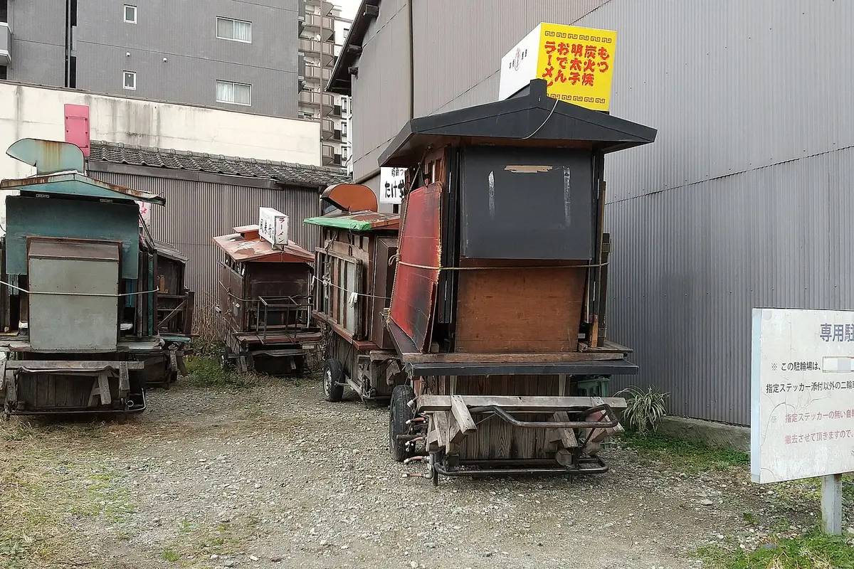 Wooden yatai carts on rubber tyres parked side by side in a gravel lot in Fukuoka in daylight