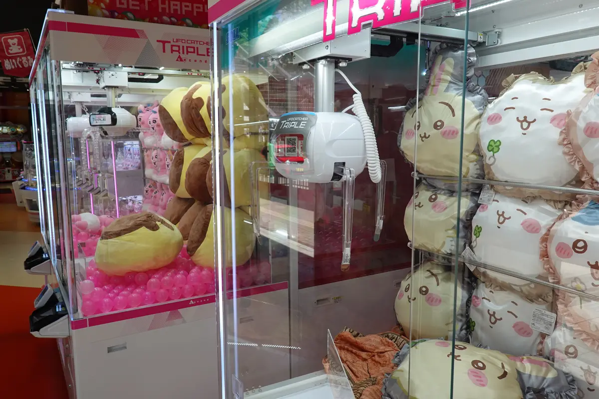 Two claw machine cabinets in a Japanese arcade, the claw arm hanging above stacked plush prizes behind glass