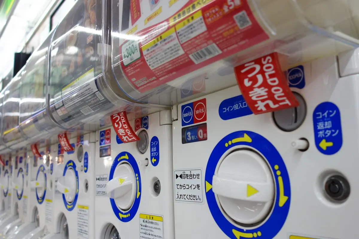 A row of Japanese capsule toy machines, each with a coin slot, a coin return button and a large white knob to turn