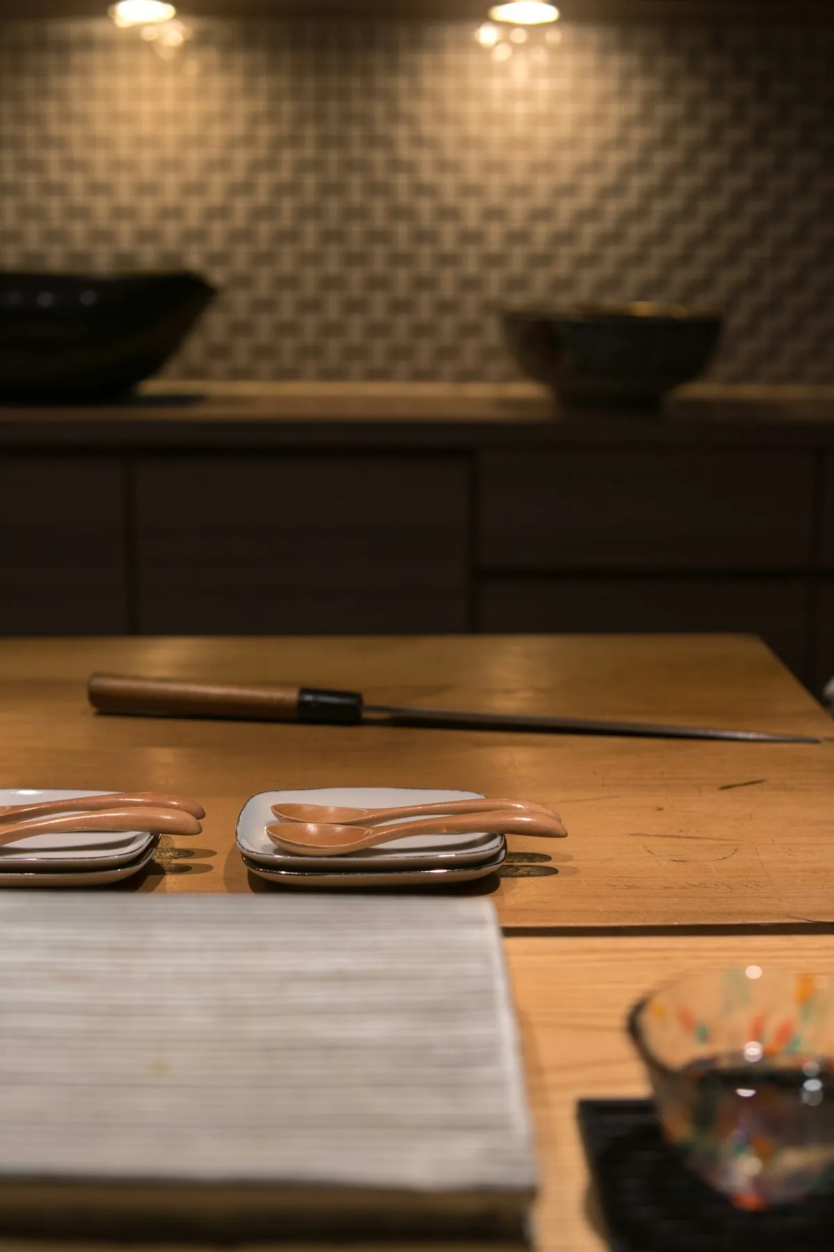 A Japanese restaurant counter with ceramic plates, wooden spoons, and bowls set for a meal
