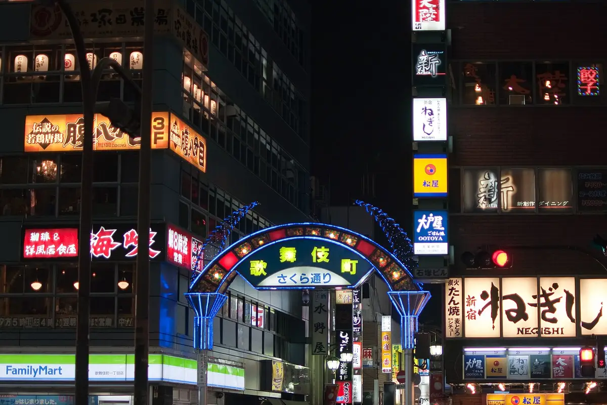 At street level in Kabukicho at night: the lit gate over Sakura-dori, between signs for a convenience store and chain restaurants