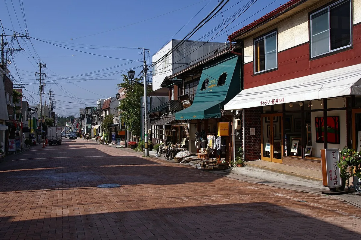 A quiet brick-paved stretch of Kyu-Karuizawa Ginza with small shopfronts and green trees under a clear sky