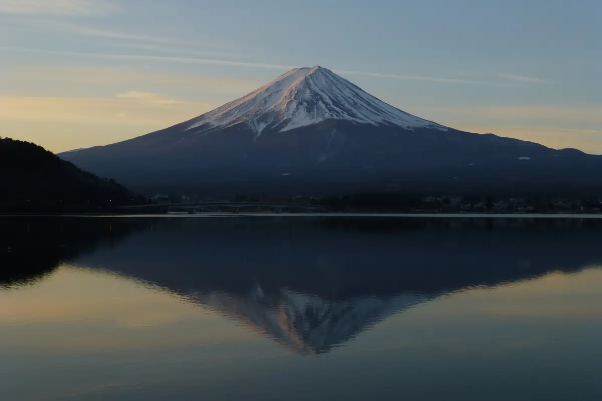 From the shore of Lake Kawaguchi in January: the whole cone of Mount Fuji mirrored in water without a ripple, the lakeside town a dark line between them