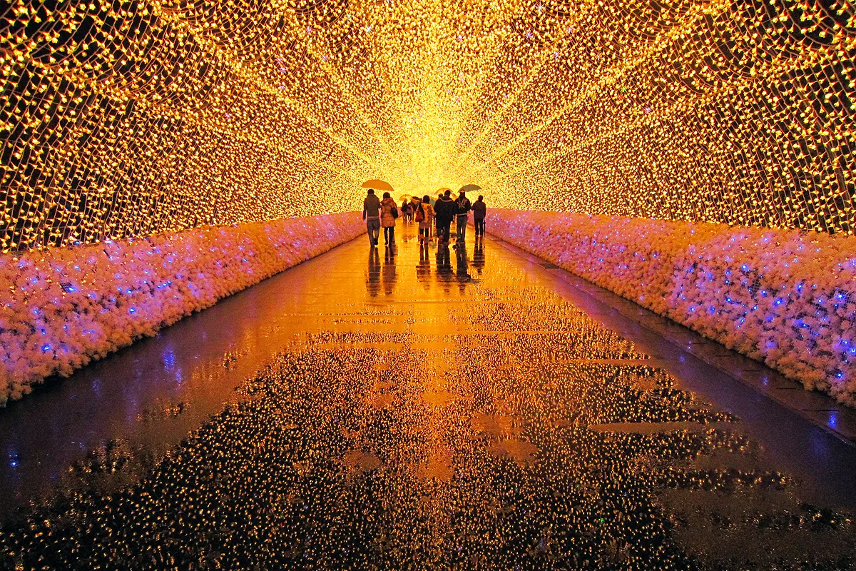 Visitors walking through a long illuminated tunnel of warm white and colored lights at Nabana no Sato in winter