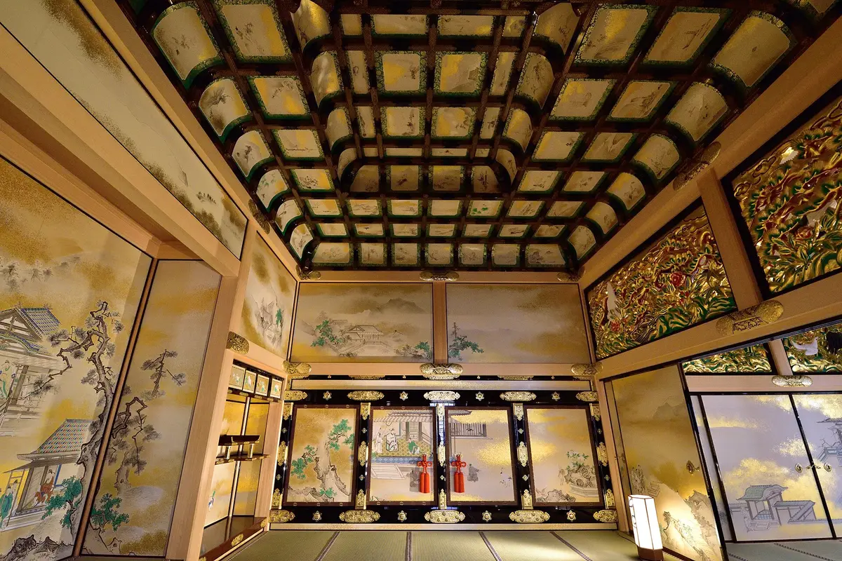Inside the rebuilt Hommaru Palace: a tatami room with a coffered ceiling of painted panels, gilded openwork transoms, and sliding doors painted on a gold ground with decorative metal fittings