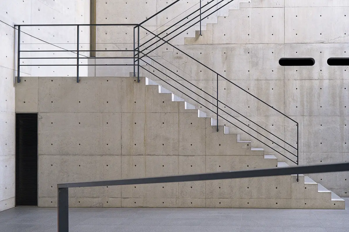 An empty concrete stair with a slim steel handrail inside one of Tadao Ando's concrete buildings on Naoshima, the walls left as raw formed concrete