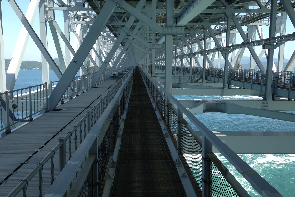 The Uzu no Michi walkway seen down its length, with mesh side panels and small glass floor windows set into the deck near the railing