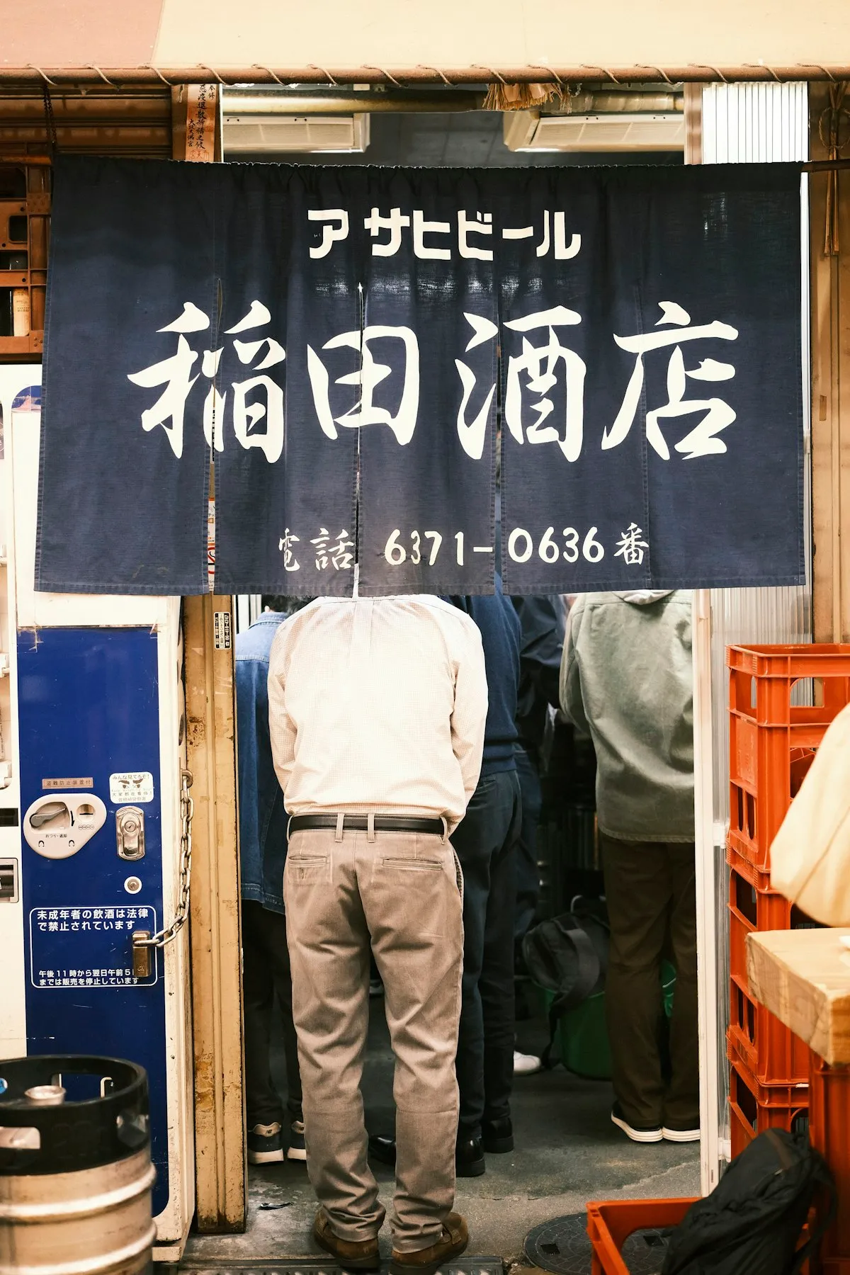 A man entering a traditional Japanese sake shop through a dark blue noren curtain