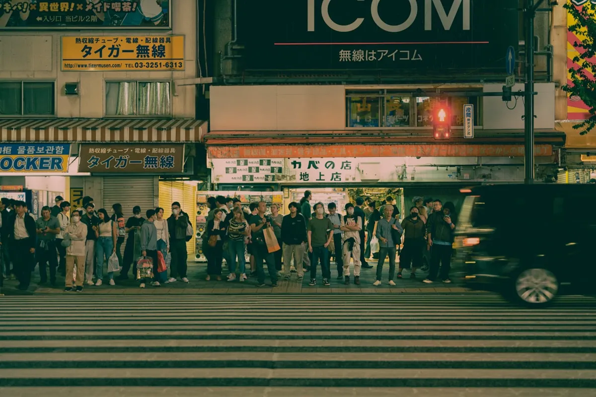A group of people waiting patiently at a crosswalk in a Japanese city at night