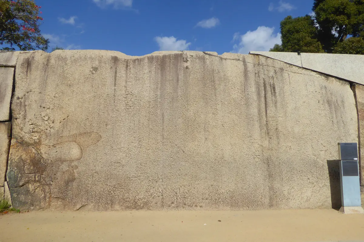 The Tako-ishi at Osaka Castle: one vast flat granite face filling the wall beside the Sakura Gate, with an information panel standing at its right