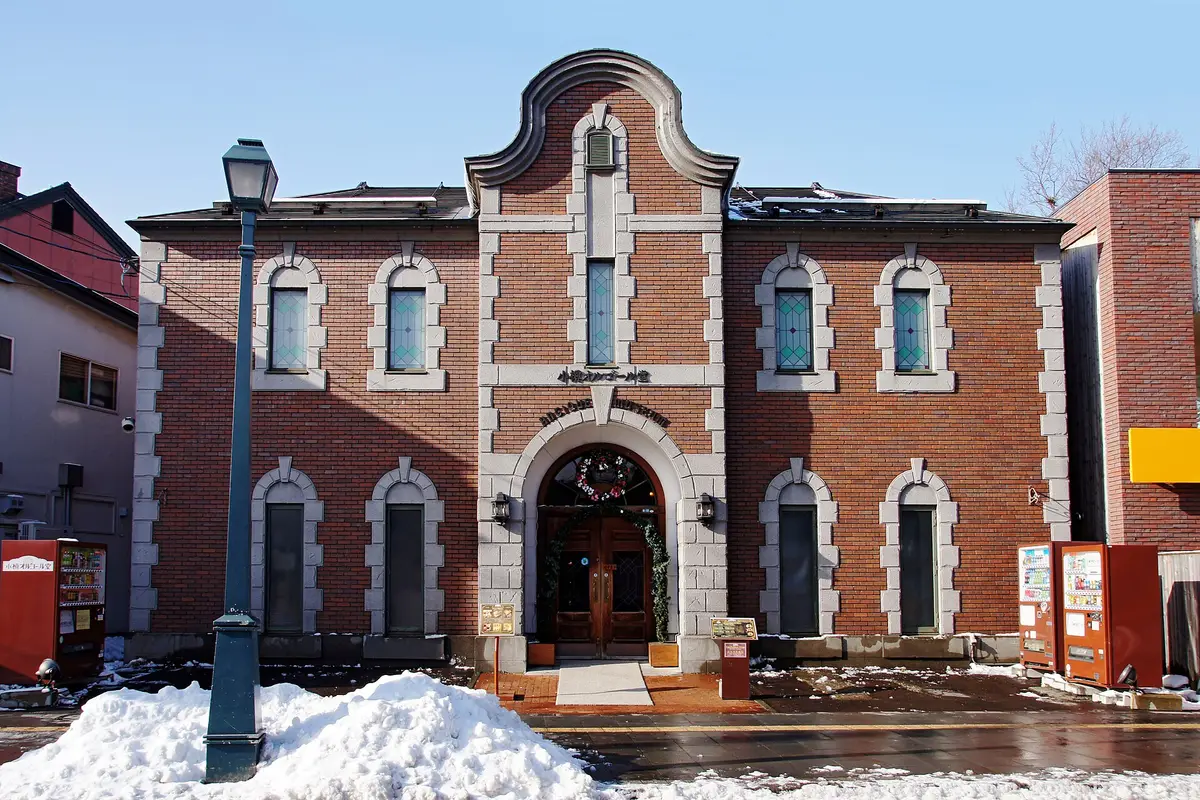 A red brick building with an arched wooden doorway on Sakaimachi Street in Otaru, the music box hall sign above the door and snow banked along the pavement