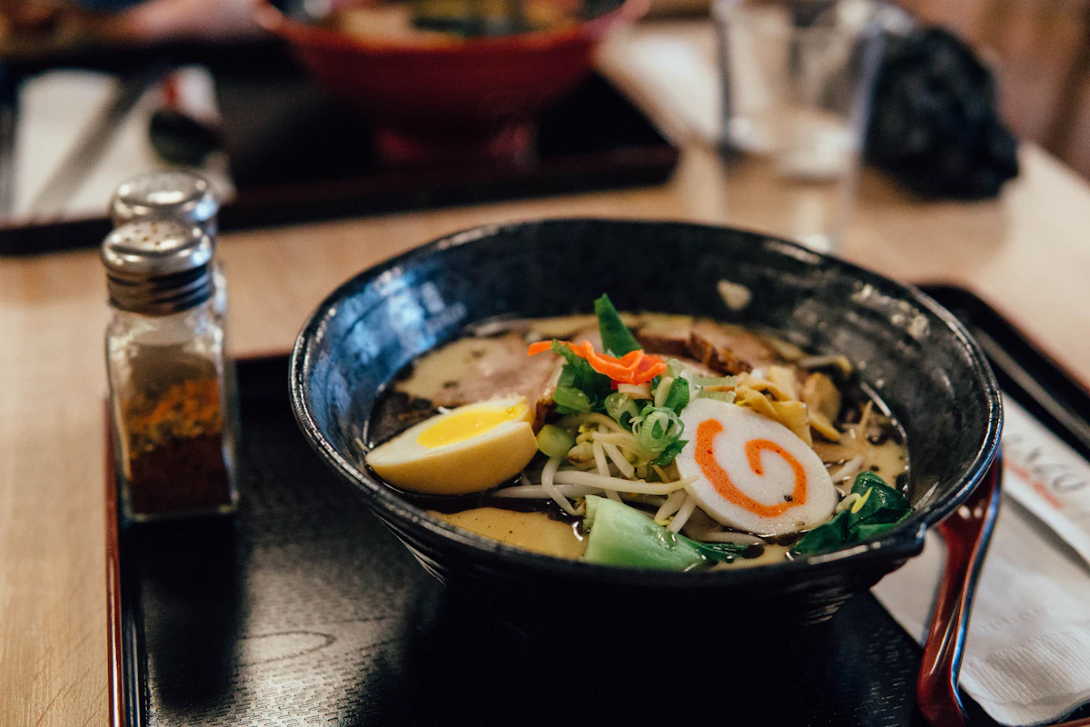 A steaming bowl of ramen with toppings and condiments at a Japanese restaurant counter