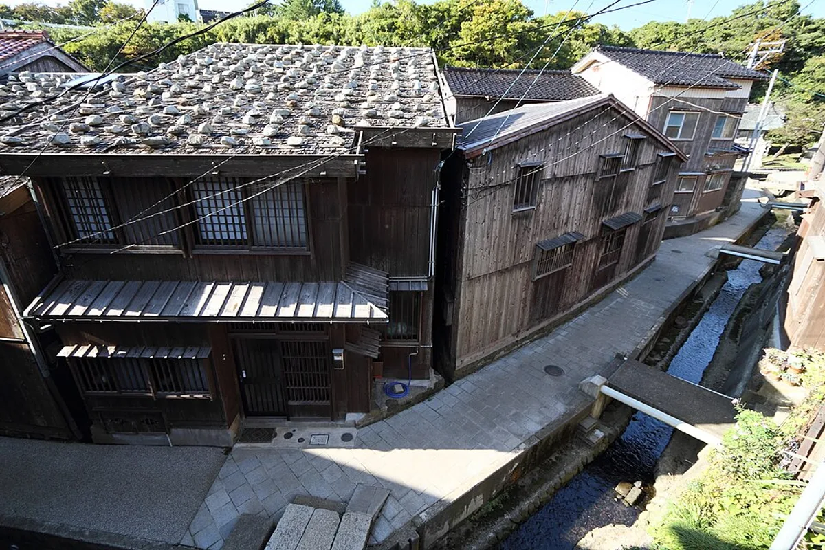 A narrow stone lane running between weathered wooden ship-plank houses in Shukunegi village, Sado Island