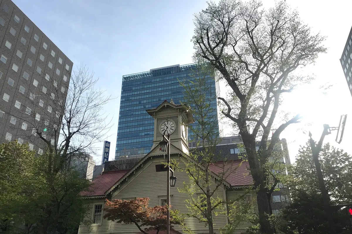 Seen from street level: the wooden Sapporo Clock Tower, with a glass office tower rising directly behind it