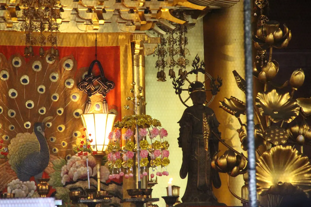 Looking into the inner altar of Senso-ji's Main Hall: gold leaf, a lit offering lamp, gilded lotus flowers and a standing bronze figure