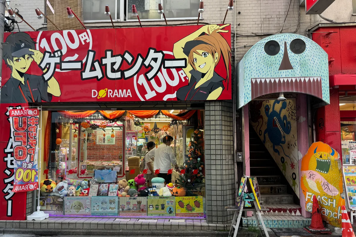 A small, brightly painted arcade and game center storefront on a Shimokitazawa side street, with signage and plush toy prizes in the window