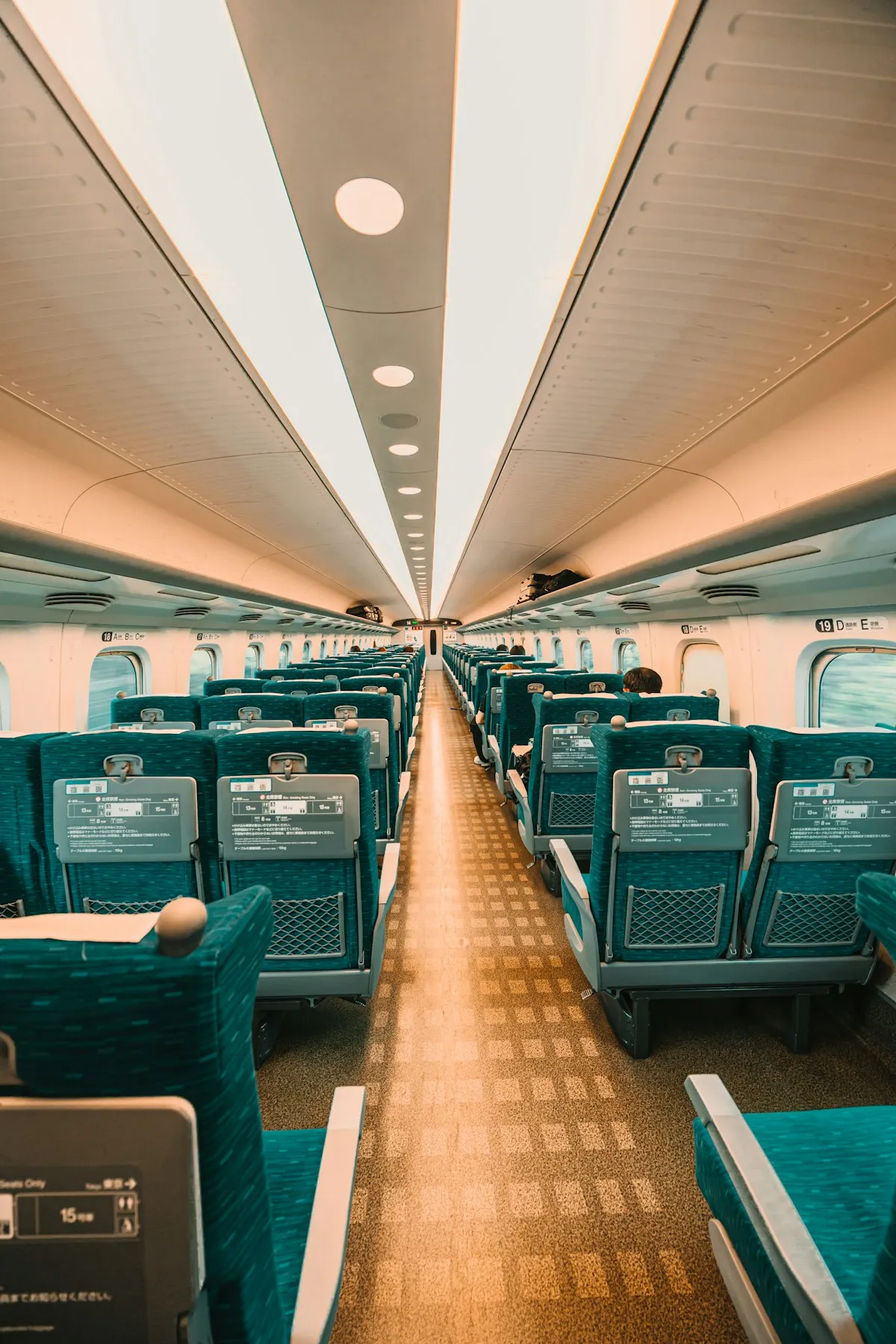The quiet interior of a Japanese Shinkansen bullet train with rows of green seats stretching into the distance
