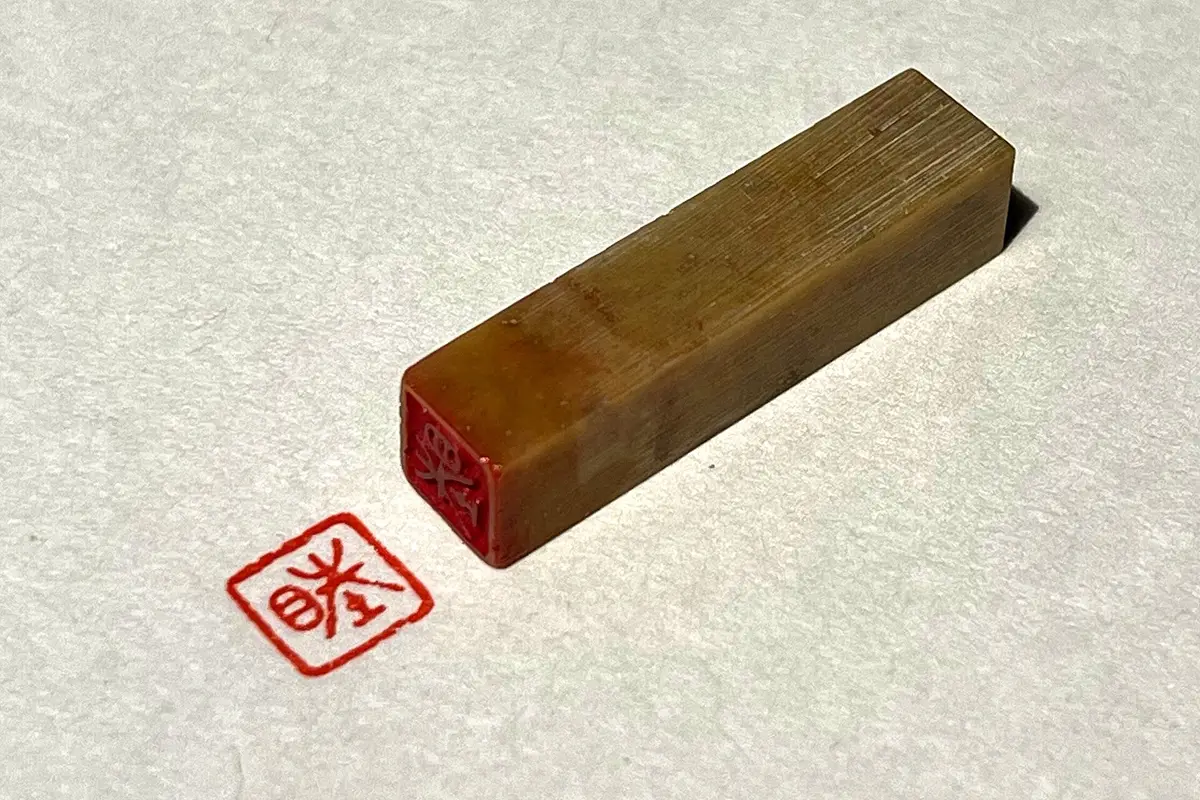 A small carved seal resting on paper beside the square red imprint it has just left