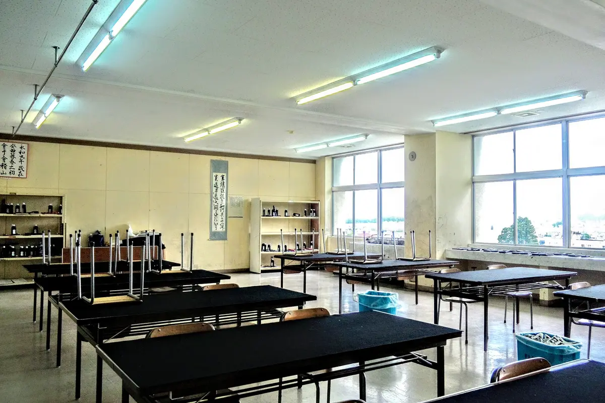 An empty calligraphy room in a Japanese school, with black-topped tables, ink bottles on open shelves and a hanging scroll on the wall