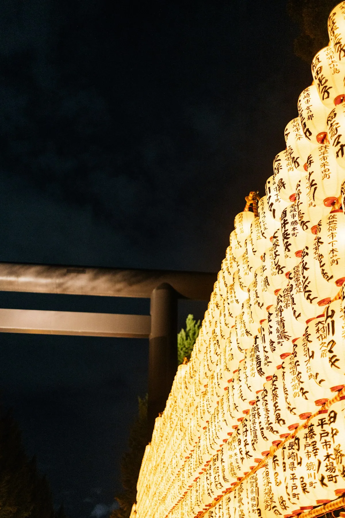 Rows of illuminated paper lanterns with Japanese calligraphy glowing beside a shrine torii gate at night