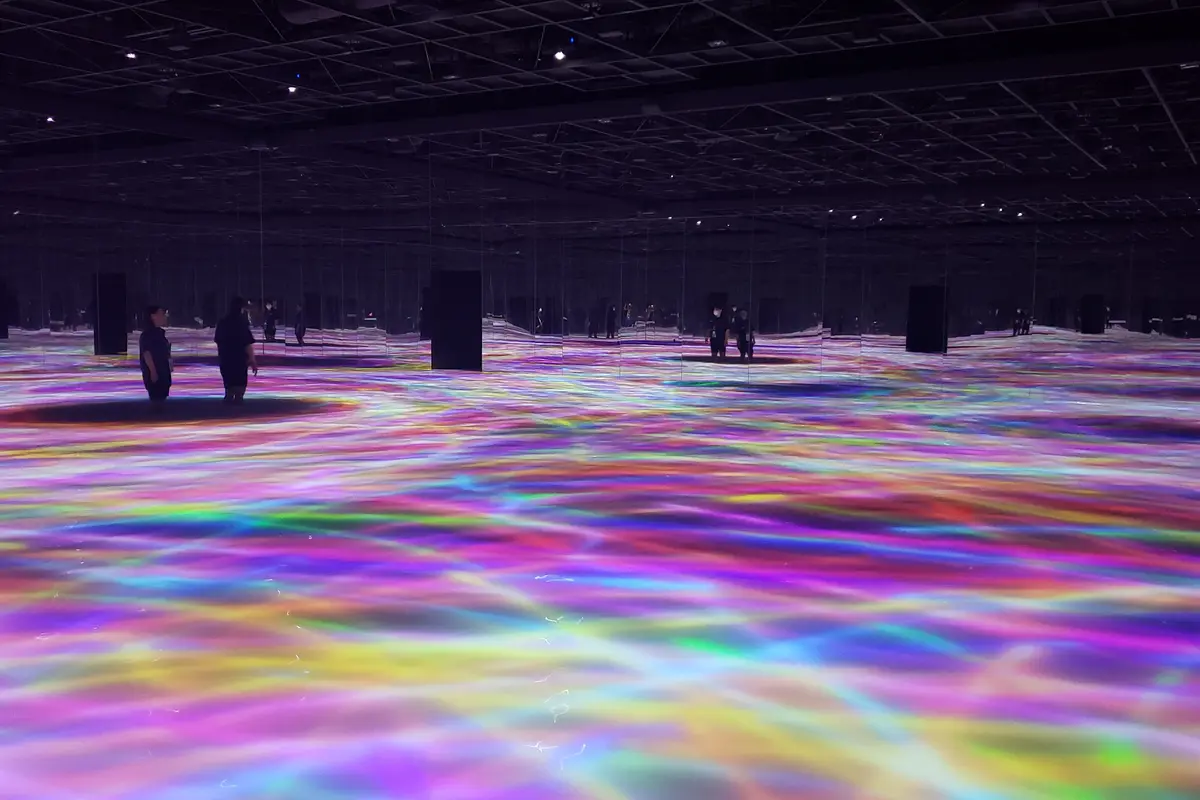 Seen from the far side of the room: colored light flowing across the entire floor at teamLab Planets in Tokyo, with a few visitors standing far apart in it