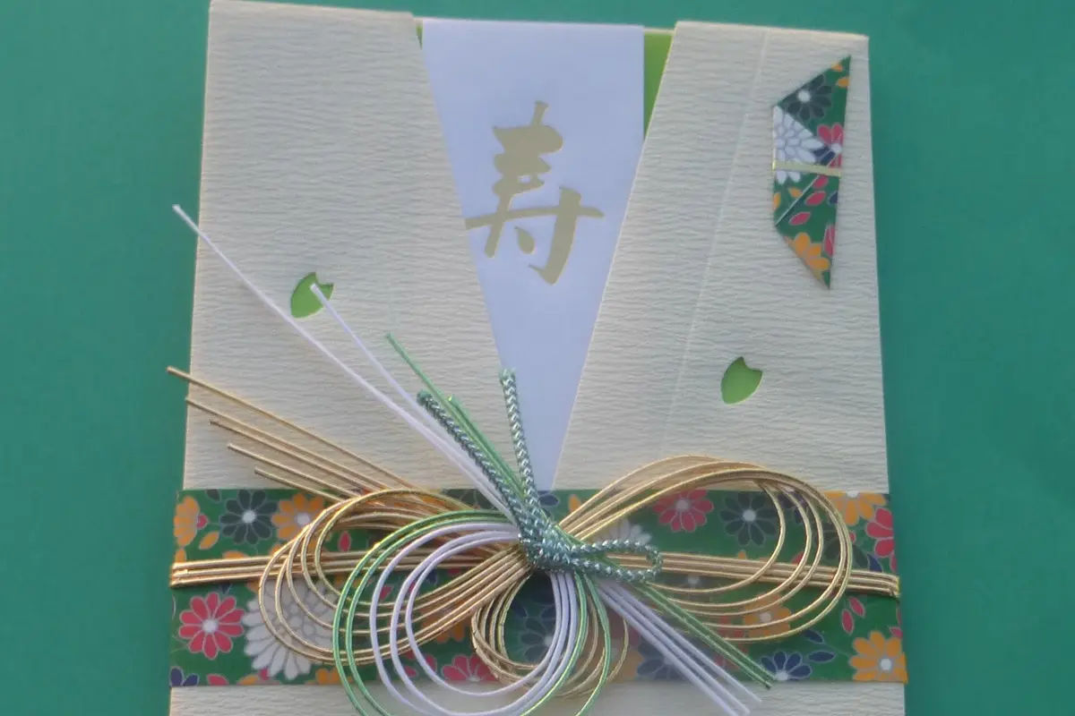 A Japanese gift envelope of textured cream paper, tied with gold, white and green mizuhiki cords in a decorative knot