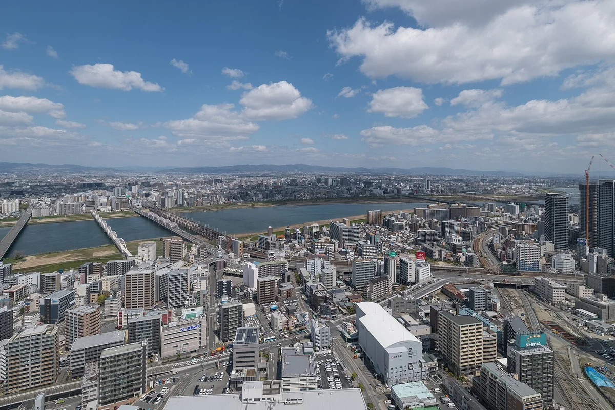 Aerial daytime view from the observatory of the Yodo River cutting through Osaka's cityscape, with distant mountains on the horizon