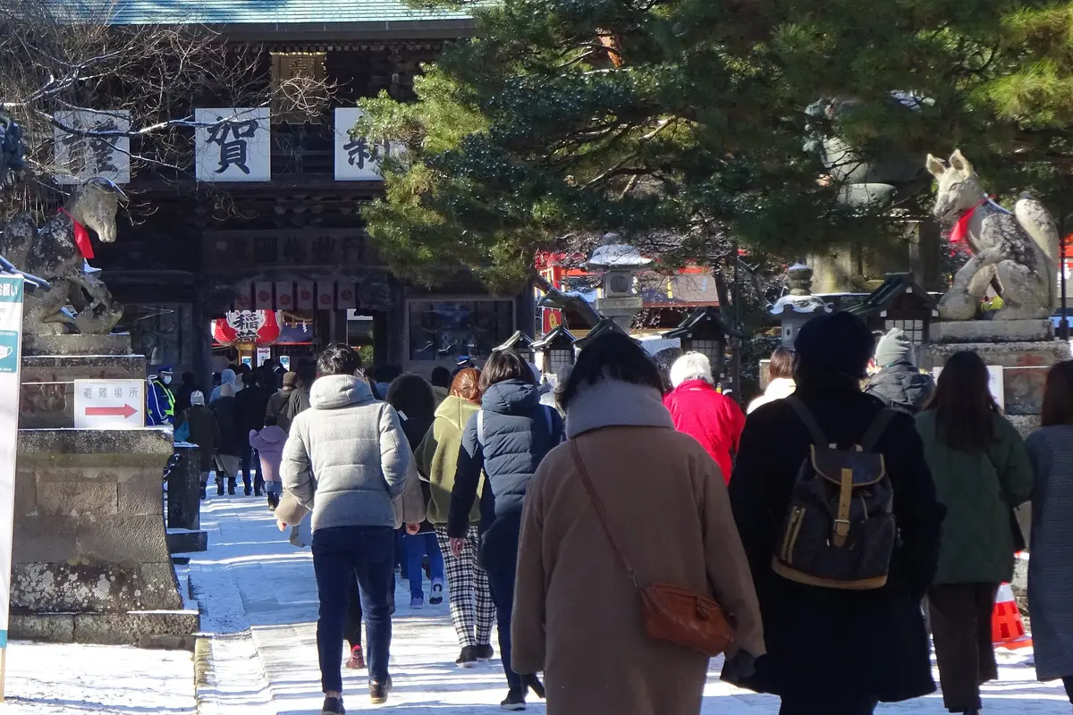Visitors seen from behind walking up a snowy shrine approach toward the gate on New Year's Day