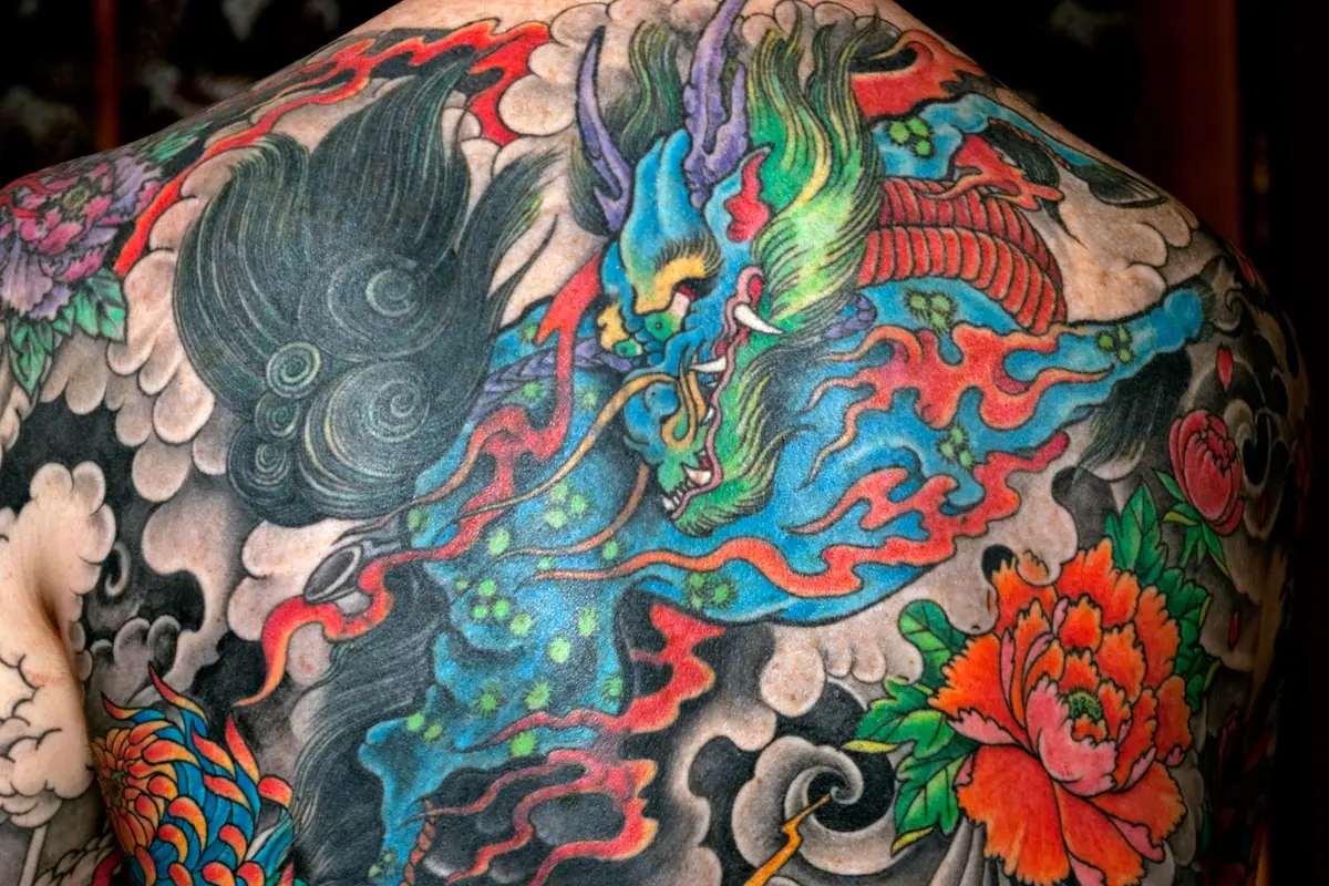 A full back covered by a Japanese-style tattoo of a dragon among clouds, with peony and chrysanthemum blossoms