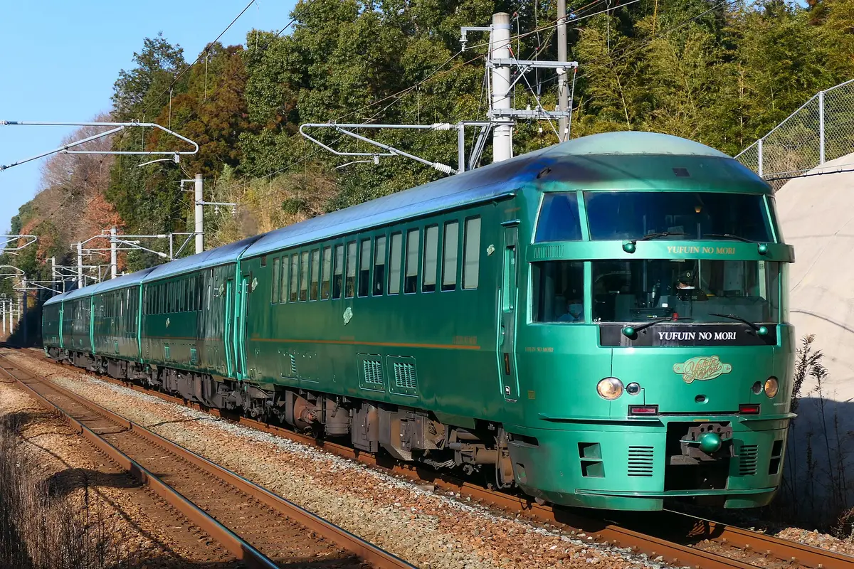 The green Yufuin no Mori limited express seen from the side as it runs along the track, its rounded front car leading