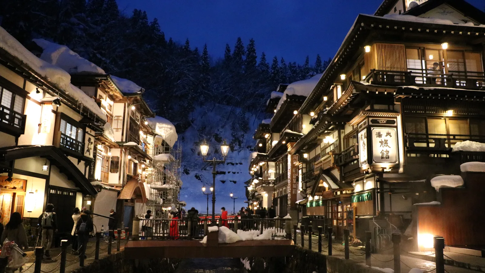 Gas lamps lit at dusk along the Ginzan River, the wooden inns glowing gold above the water