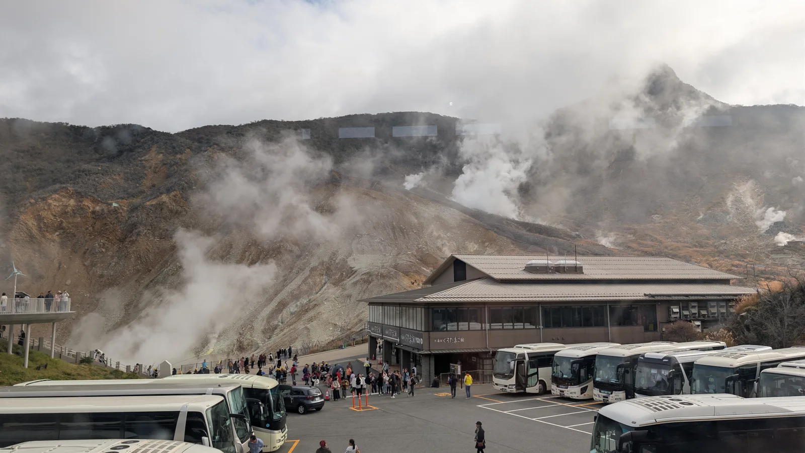 Steam rising from the bare, sulfur-streaked slopes of Owakudani, with the valley's egg house and tour buses below