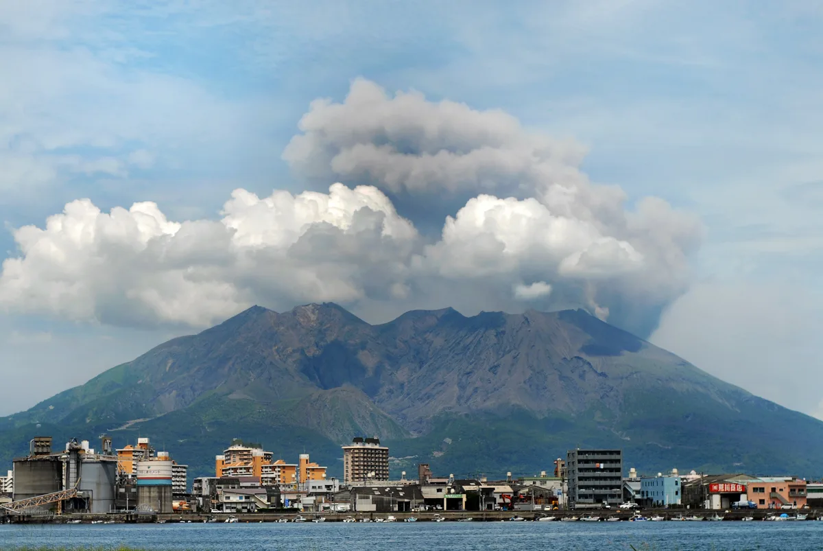 Sakurajima seen across Kinko Bay from Kagoshima, a plume of pale ash rising from the volcano above the city waterfront