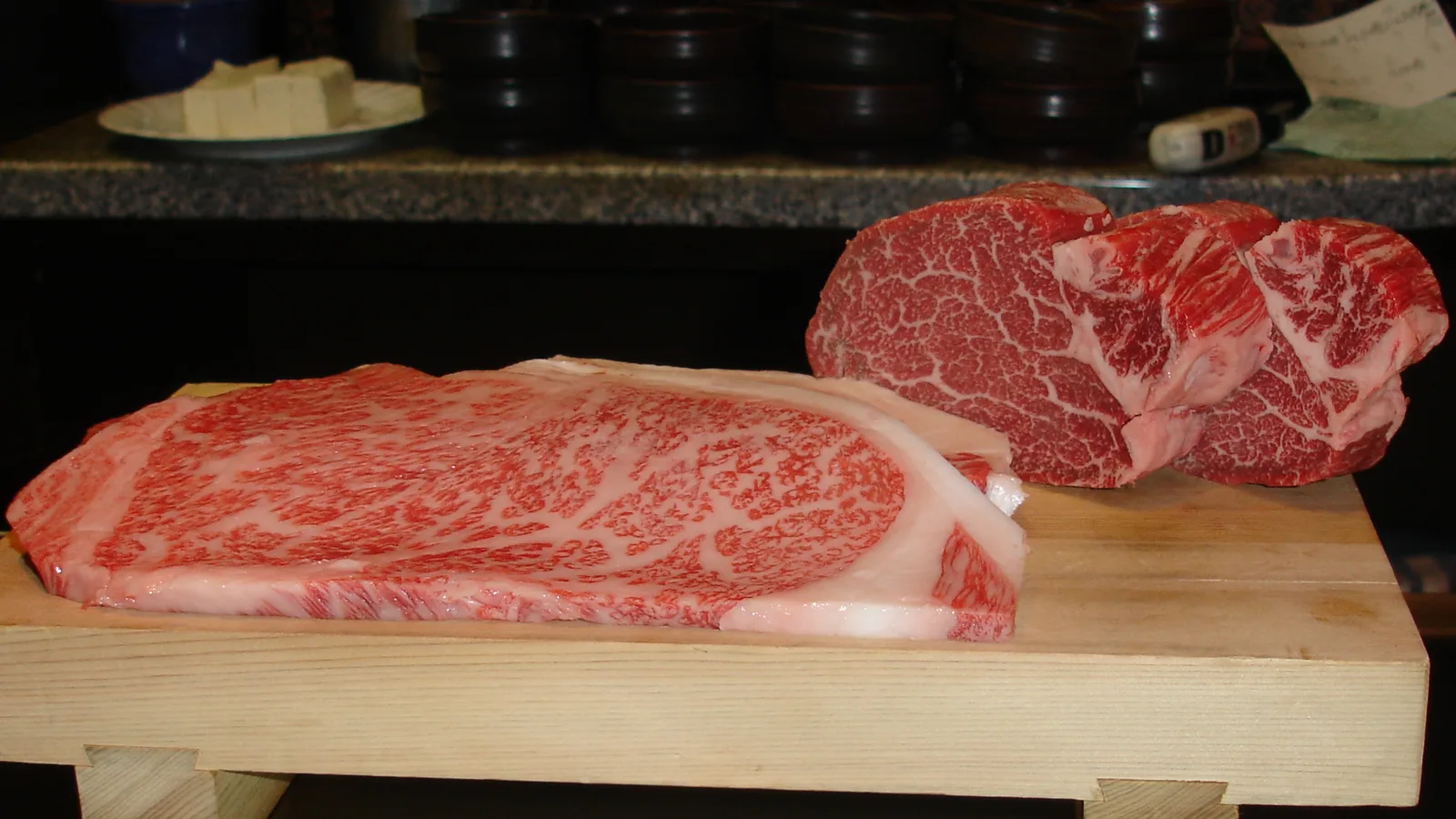 Marbled cuts of Kobe beef on a wooden block, showing the fine fat marbling the official grade is measured by