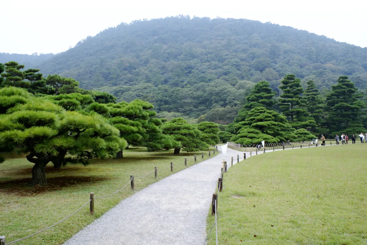 A gravel path curving through hand-pruned pines toward the wooded slope of Mt. Shiun in Ritsurin Garden