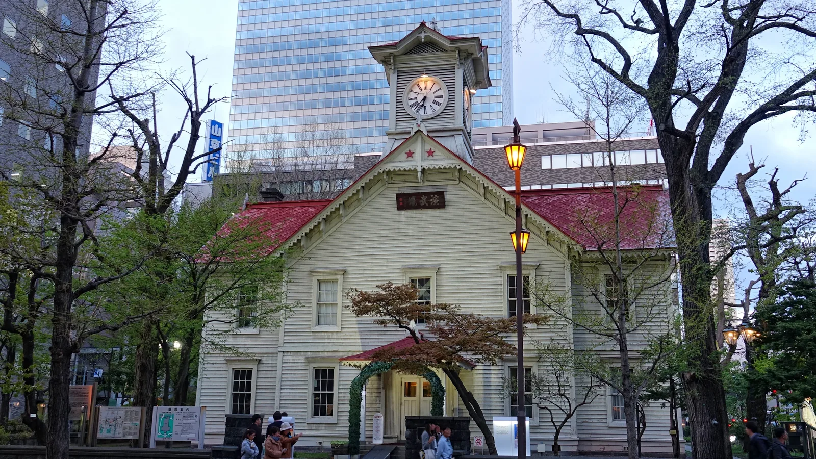 The Sapporo Clock Tower, a small white wooden hall with a clock in its gable, dwarfed by the office towers of the modern grid that grew up around it
