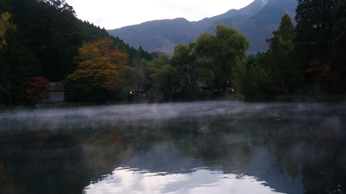 Mist rising from the surface of Lake Kinrin at dawn, with wooded hills behind