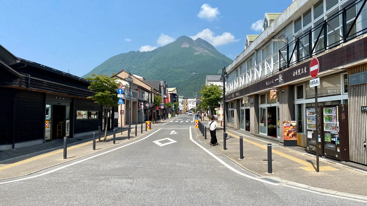 A shop-lined street in Yufuin leading toward the twin-peaked Mount Yufu on a clear day
