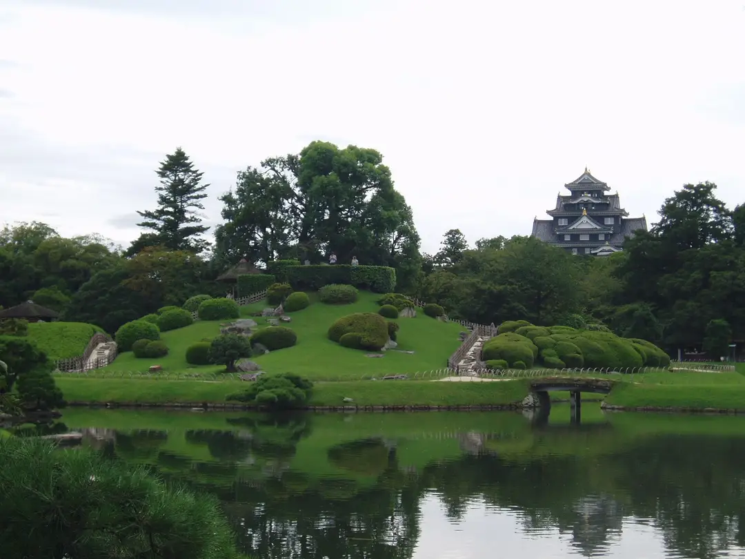 Korakuen garden in Okayama, its lawns and pond spread below the black keep of Okayama Castle across the river