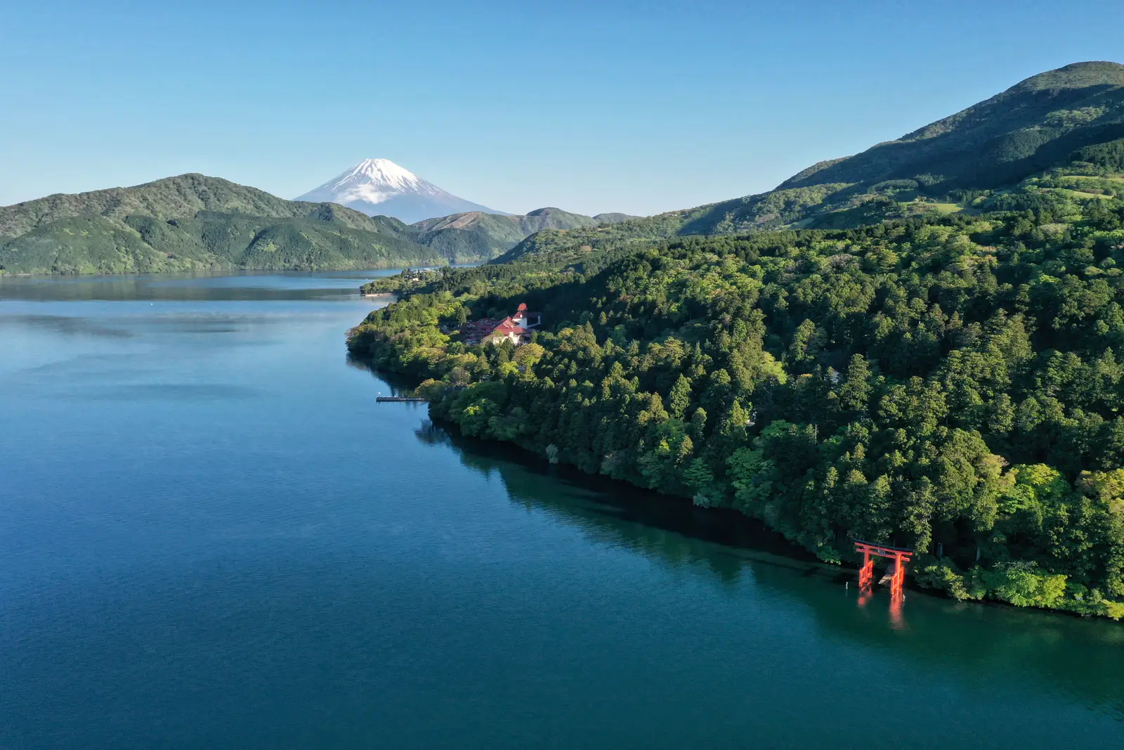 Lake Ashinoko in Hakone with the red torii gate of Hakone Shrine at the forested shore and the snow-capped peak of Mount Fuji beyond