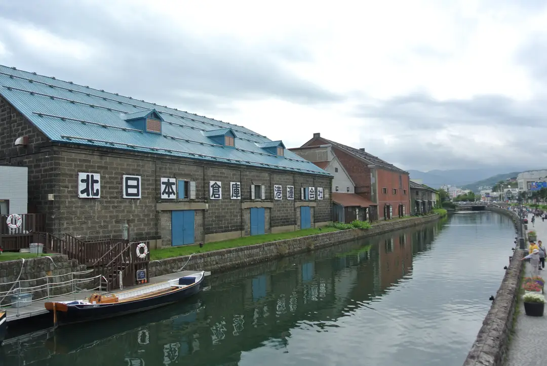 Stone warehouses lining the Otaru Canal, a small wooden boat moored at the water's edge