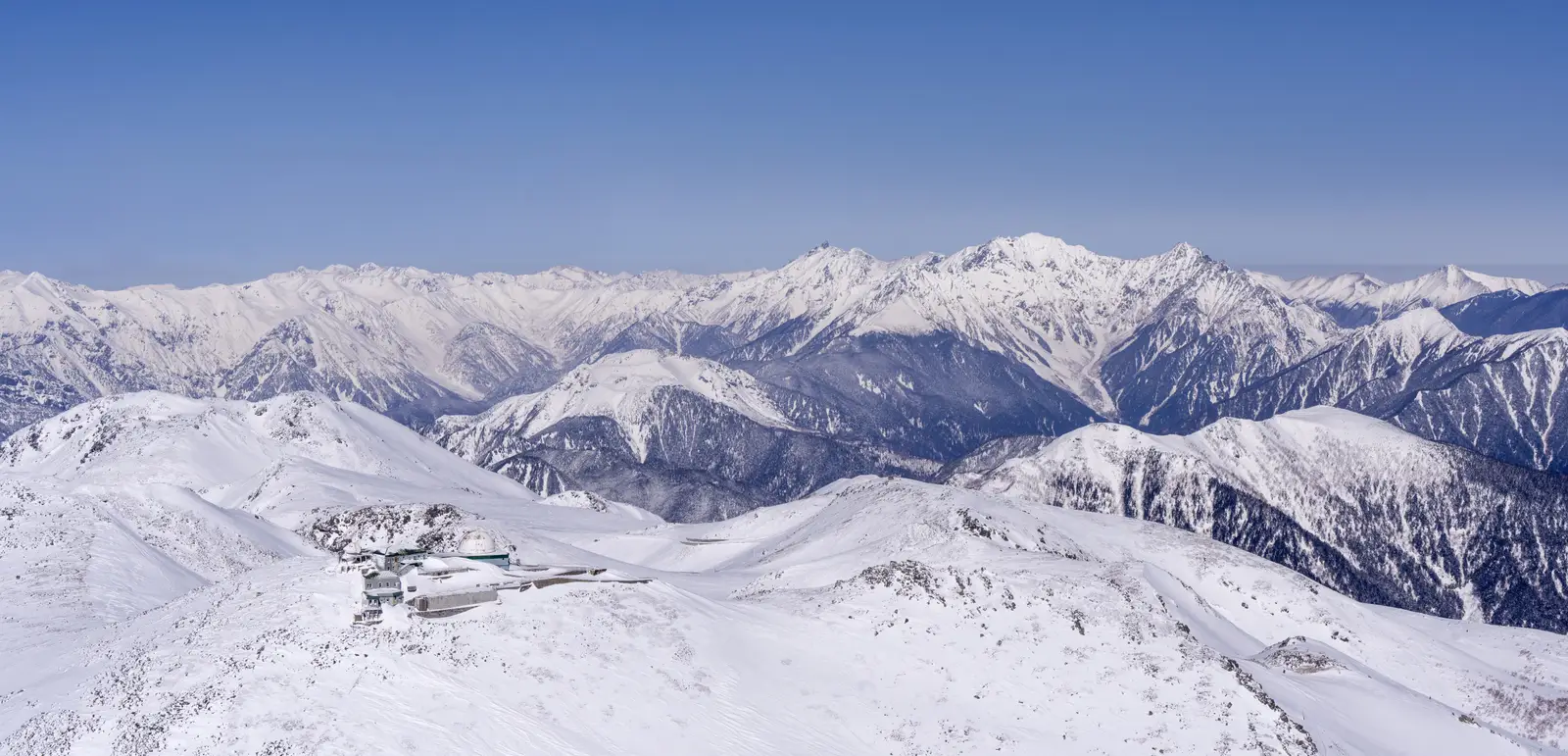 The snow-capped peaks of the Northern Japan Alps stretching to the horizon under a clear blue sky