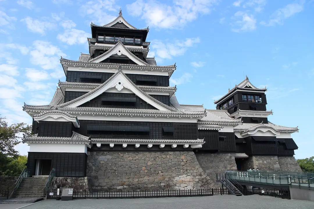 The reconstructed black-and-white keep of Kumamoto Castle rising above its great curved stone walls under a blue sky