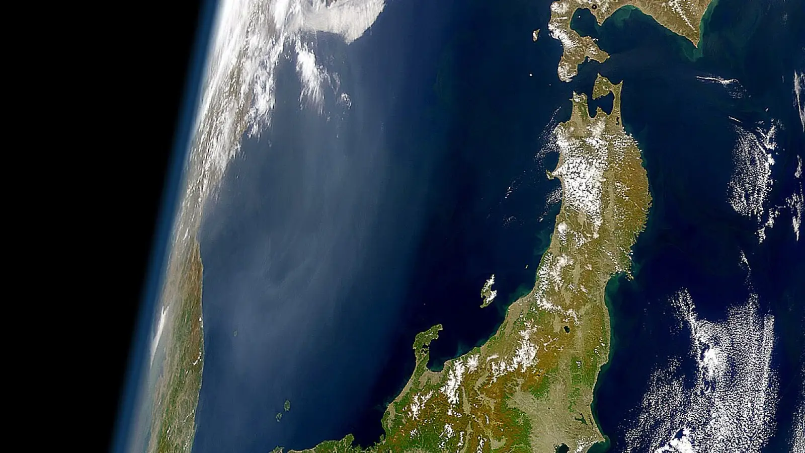 Japan seen from space, the archipelago sweeping north past Tohoku to Hokkaido under drifting cloud at the curve of the Earth